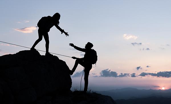 Two people helping each other climb a mountain